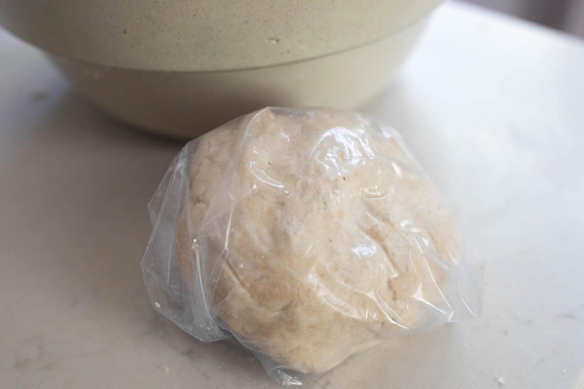 Pie dough formed into a ball and wrapped in plastic wrap on a counter top.