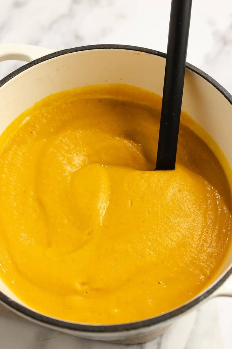 Blended roasted pumpkin soup in a large dutch oven with a black ladle.