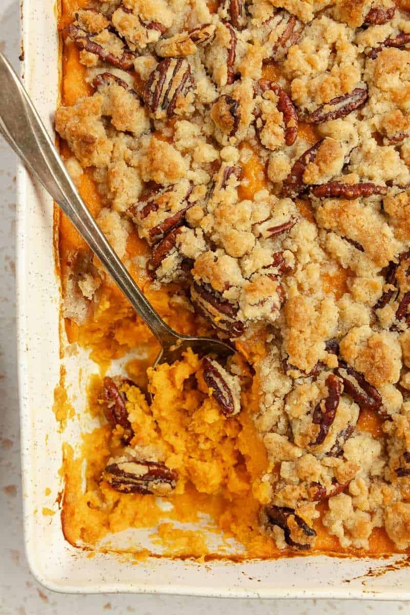 Sweet potato casserole in a baking dish with a serving missing and a big silver spoon.