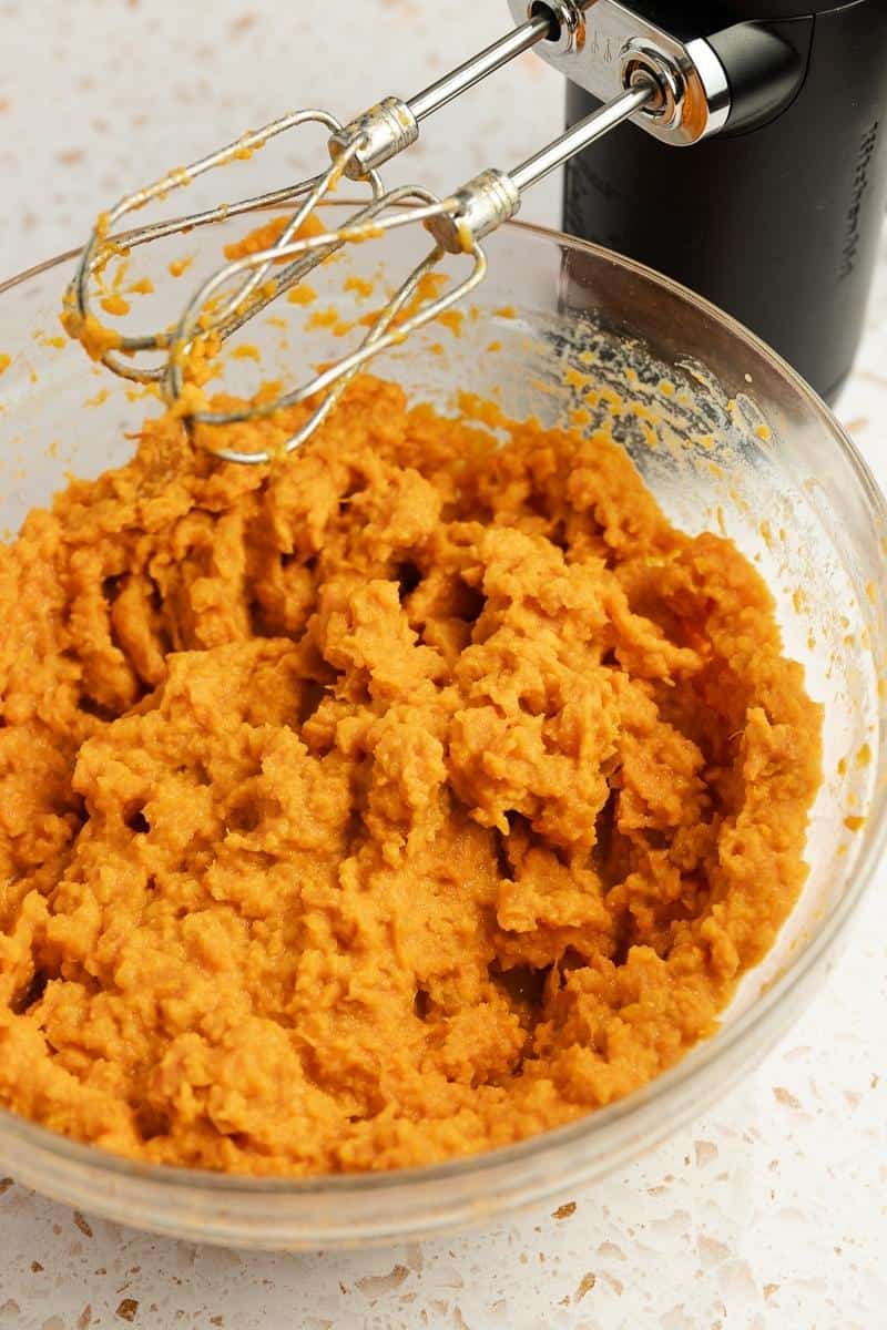 Sweet potatoes mixed with a hand mixer in a large mixing bowl with heavy cream and other ingredients.