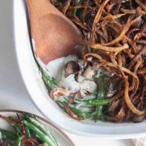 a wooden spoon in a baking dish scooping up one serving of green bean casserole.