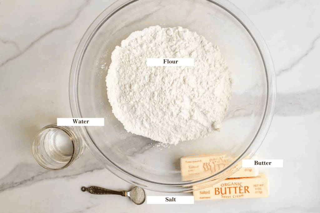 flour in a bowl, butter, water, and salt in a measuring spoon on a countertop.