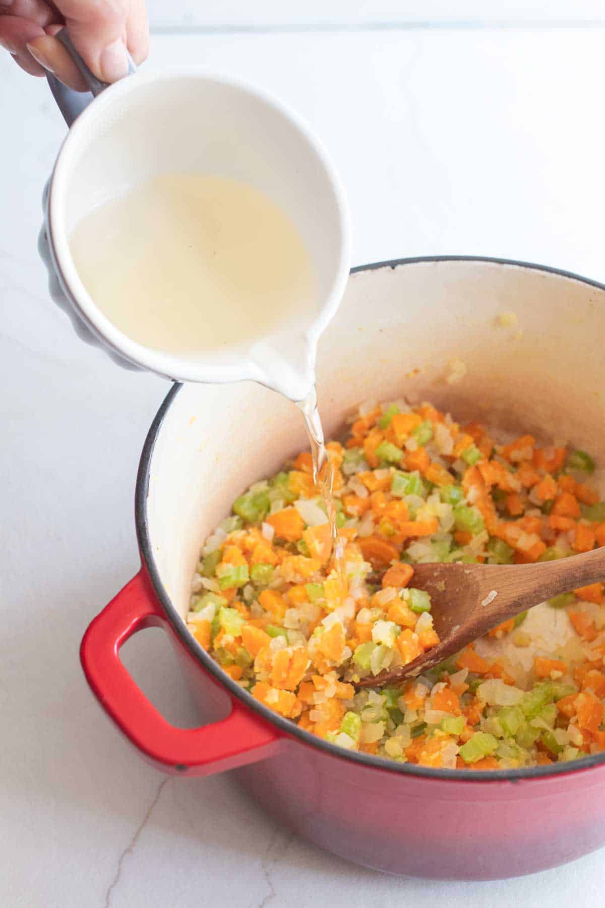 A pouring dish full of white wine being poured into a dutch oven of veggies.