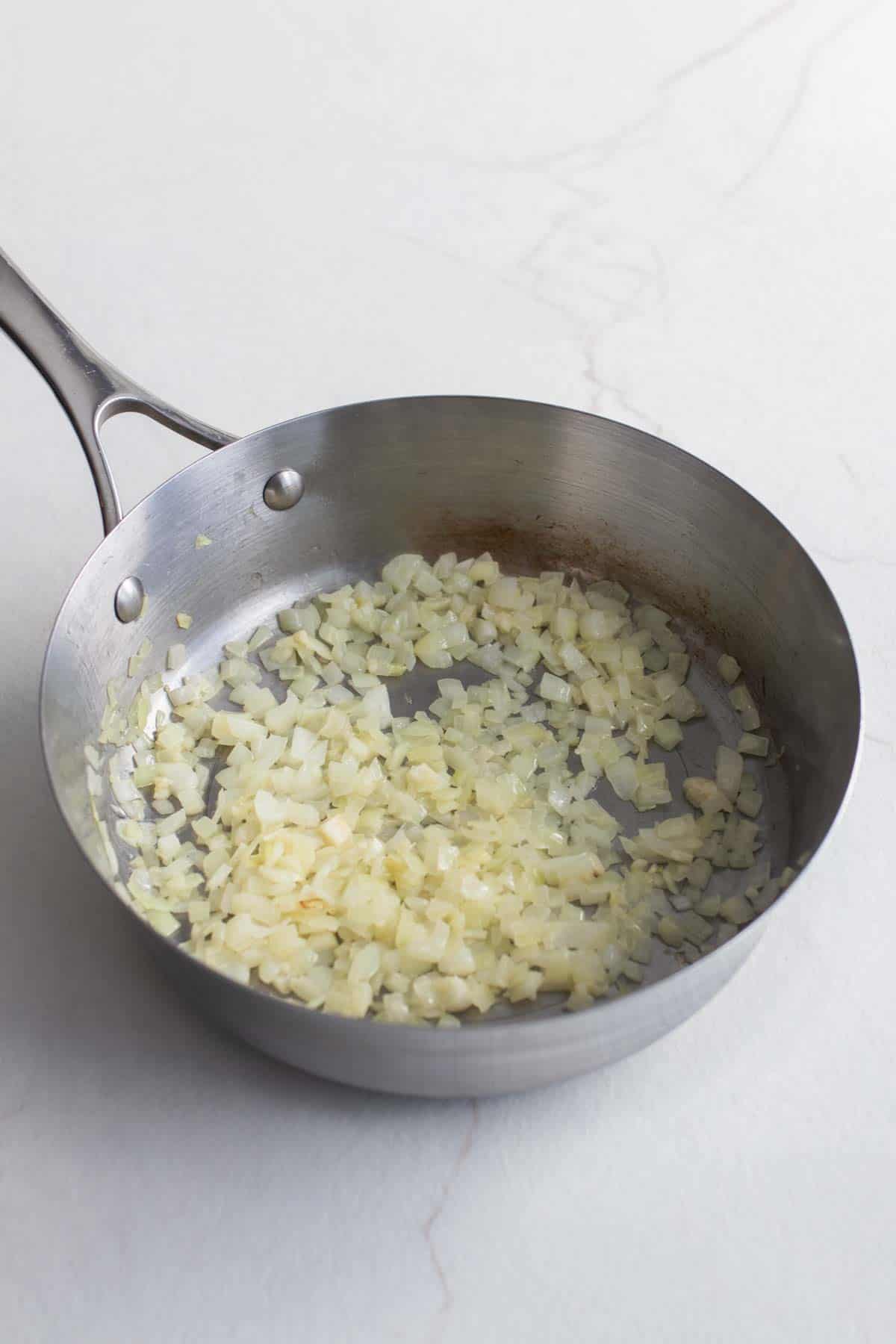 Diced onions cooking in a stainless steel pan.