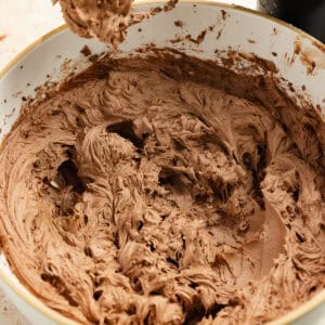 Chocolate frosting mixed in a bowl with a hand mixer next to it.