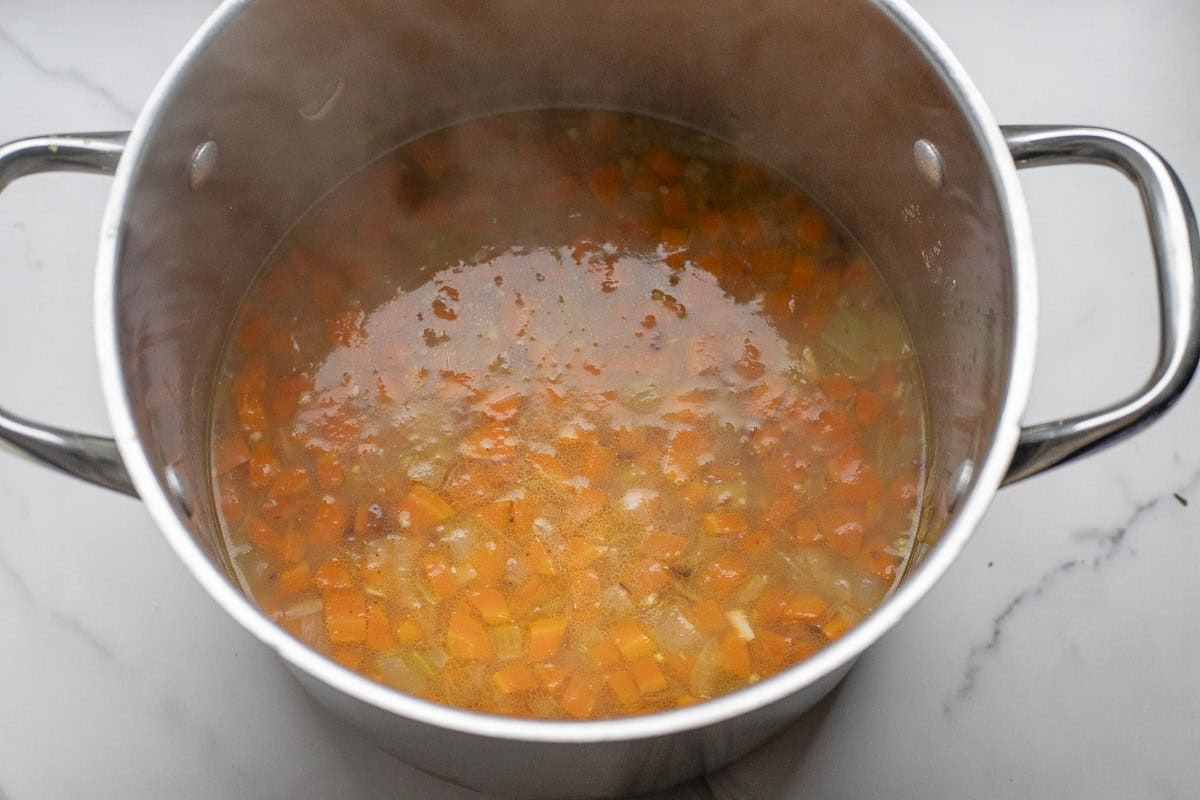 Broth added to a large stock pot of cooked diced veggies.