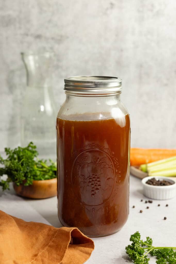 Bone broth in a half gallon mason jar with ingredients surrounding the jar.