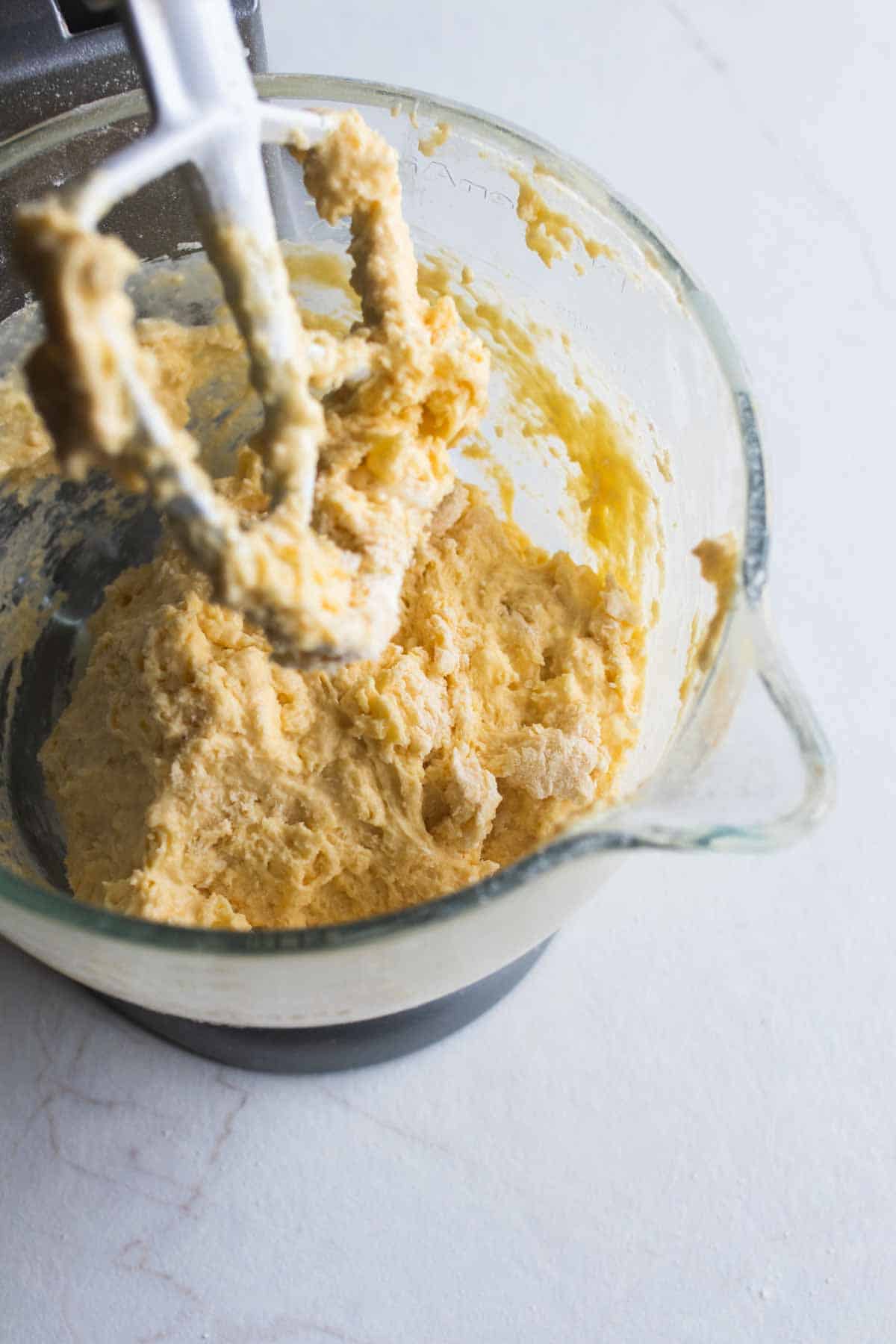 A paddle attachment lifted out of a stand mixer bowl that has wet and dry ingredients mixed together.