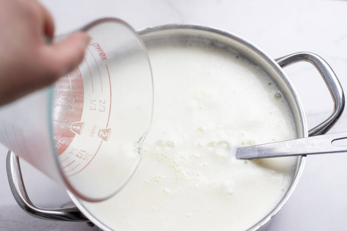 Farmers cheese on a cutting board with a glass of milk in the background.
