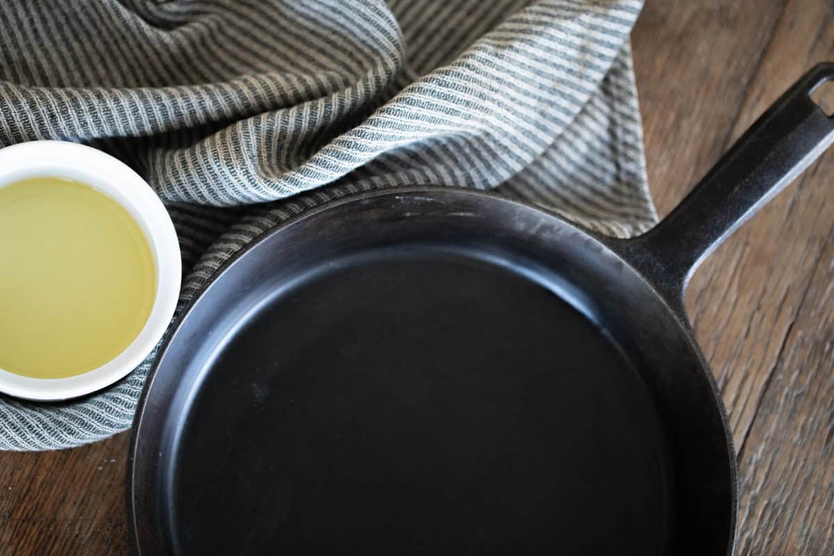 Skillet next to a bowl of oil and a tea towel.
