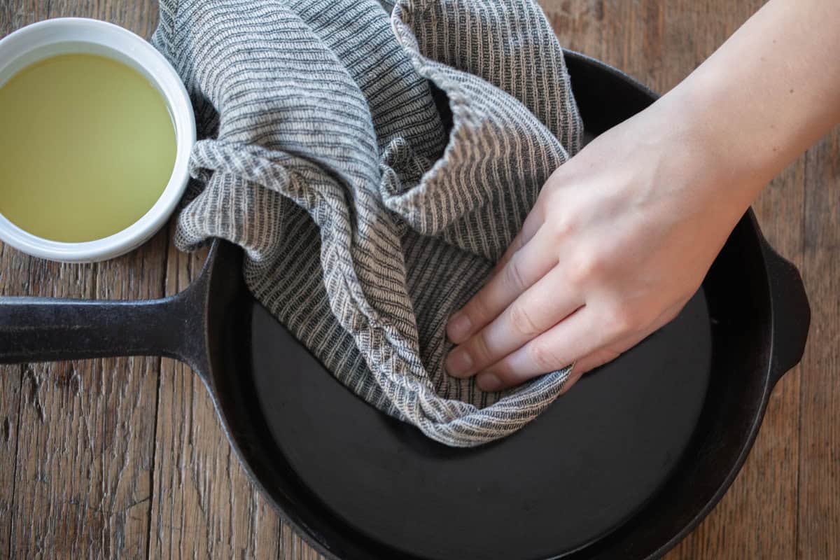 Wiping a cast iron skillet with a towel dipped in oil.