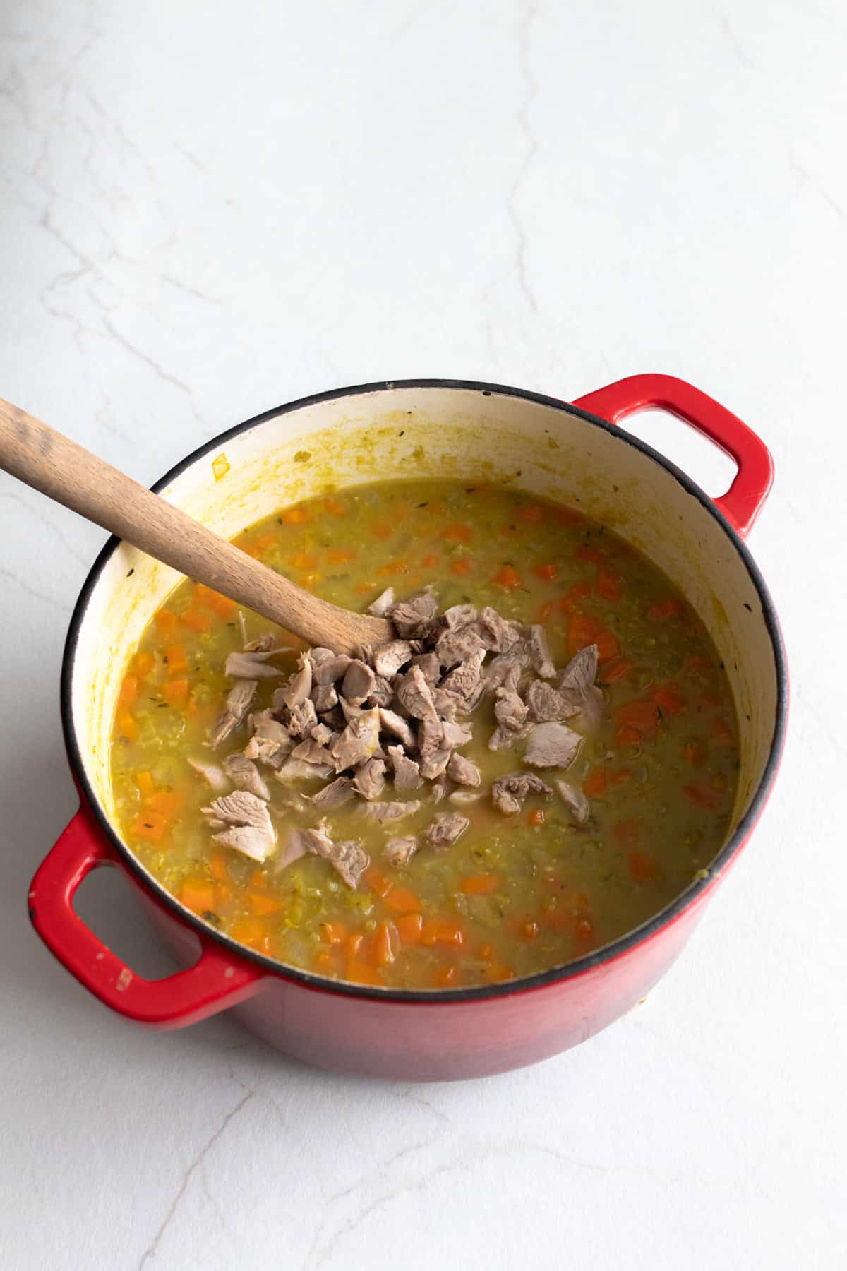 Chunks of meet added to soup pot with large wooden spoon.