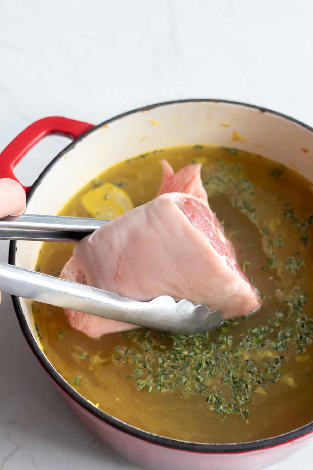 Tongs holding a hambone that is added into a large Dutch oven full of broth.
