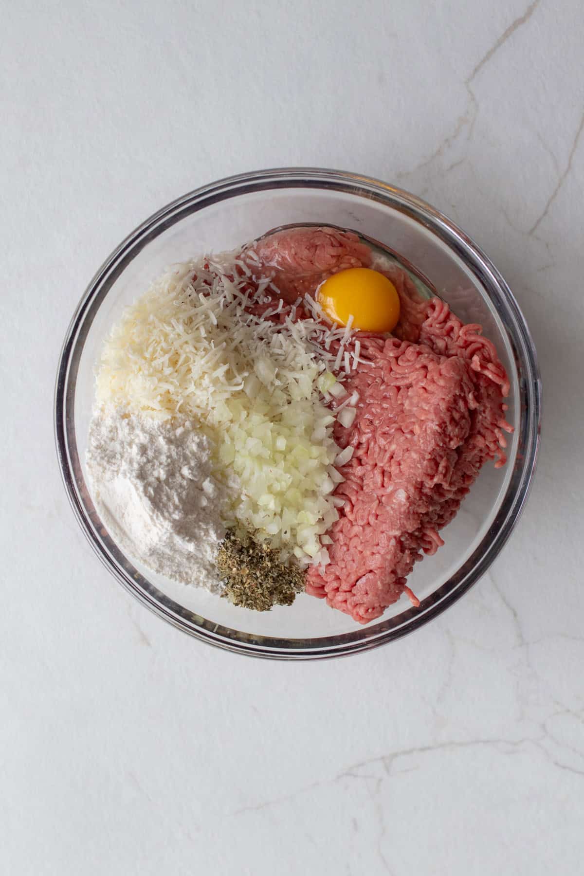 A bowl with raw ground beef, an egg, and seasonings.