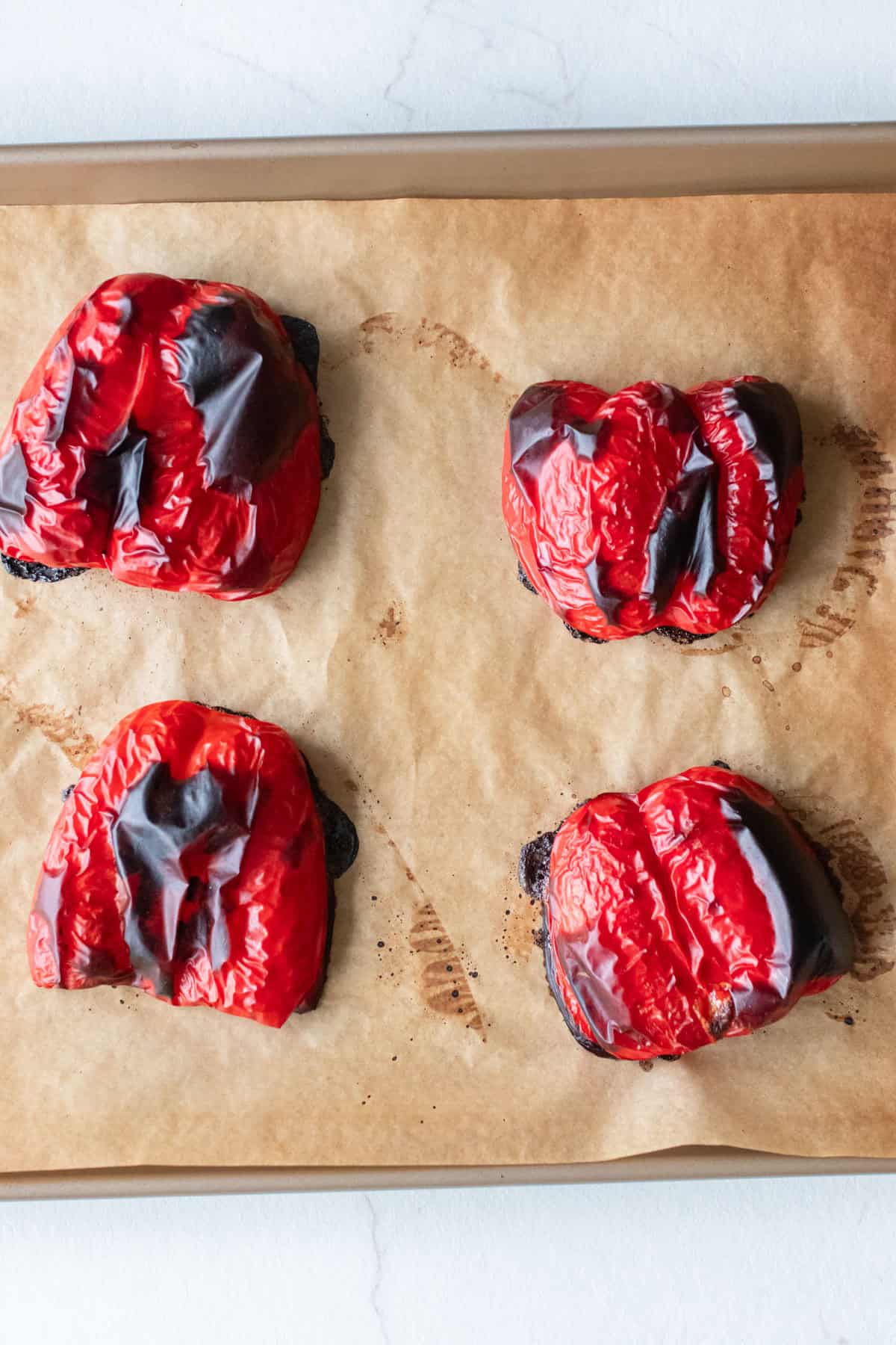 Four bell pepper halves roasted on a pan lined with parchment paper.