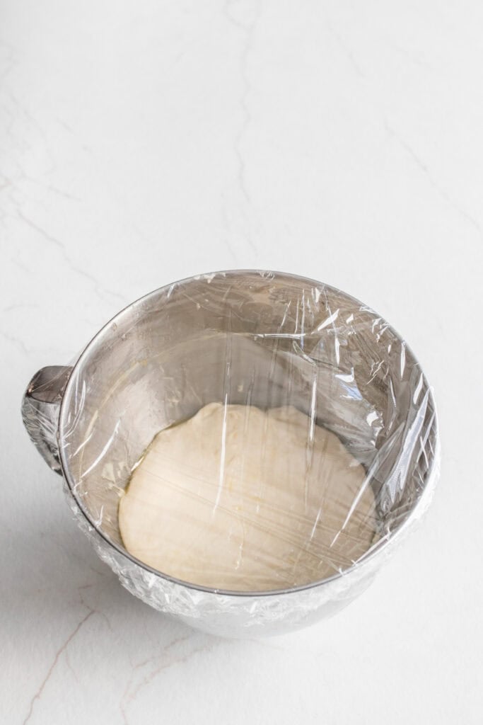 Sourdough in a stainless steel mixing bowl covered with plastic wrap to ferment.