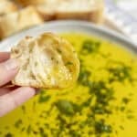 A hand holding a piece of bread dipping in oil.