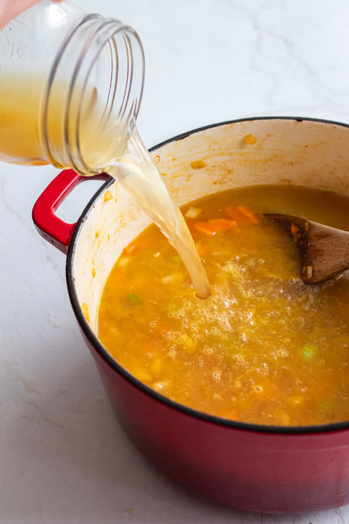 Adding broth into the sautéed vegetables.