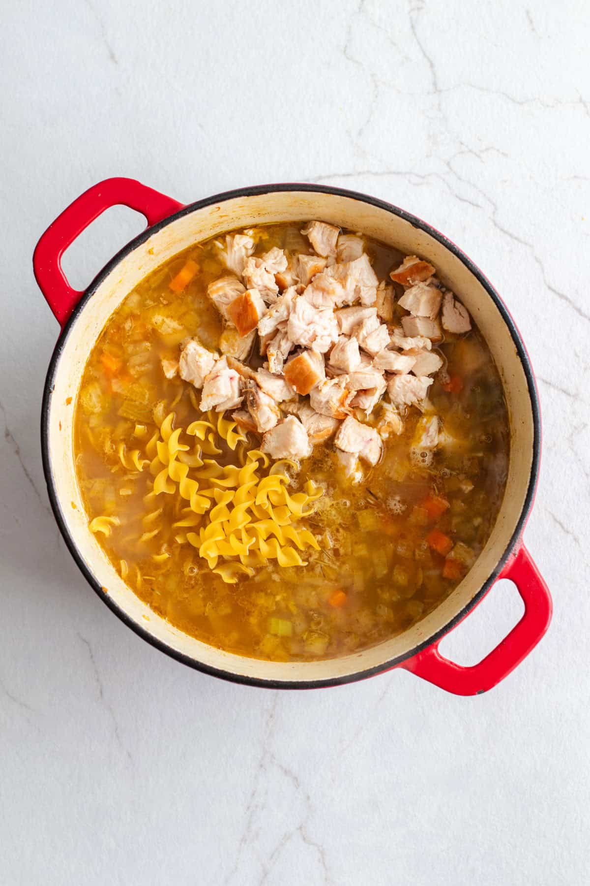 Adding chicken and noodles to a pot of broth and vegetables.