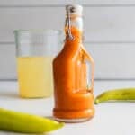 Fermented hot sauce in a jar surrounded by peppers and a jar of brine in the background.