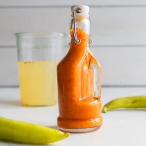 Fermented hot sauce in a jar surrounded by peppers and a jar of brine in the background.