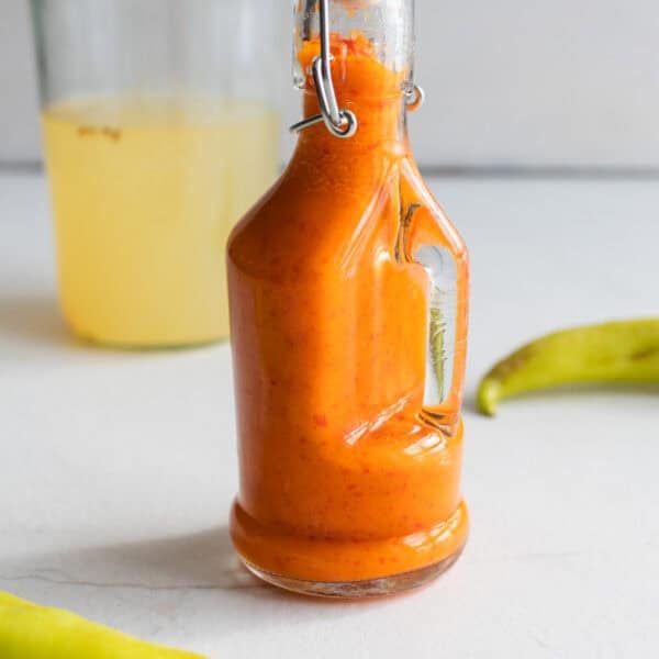 Fermented hot sauce in a swing top bottle surrounded by peppers.