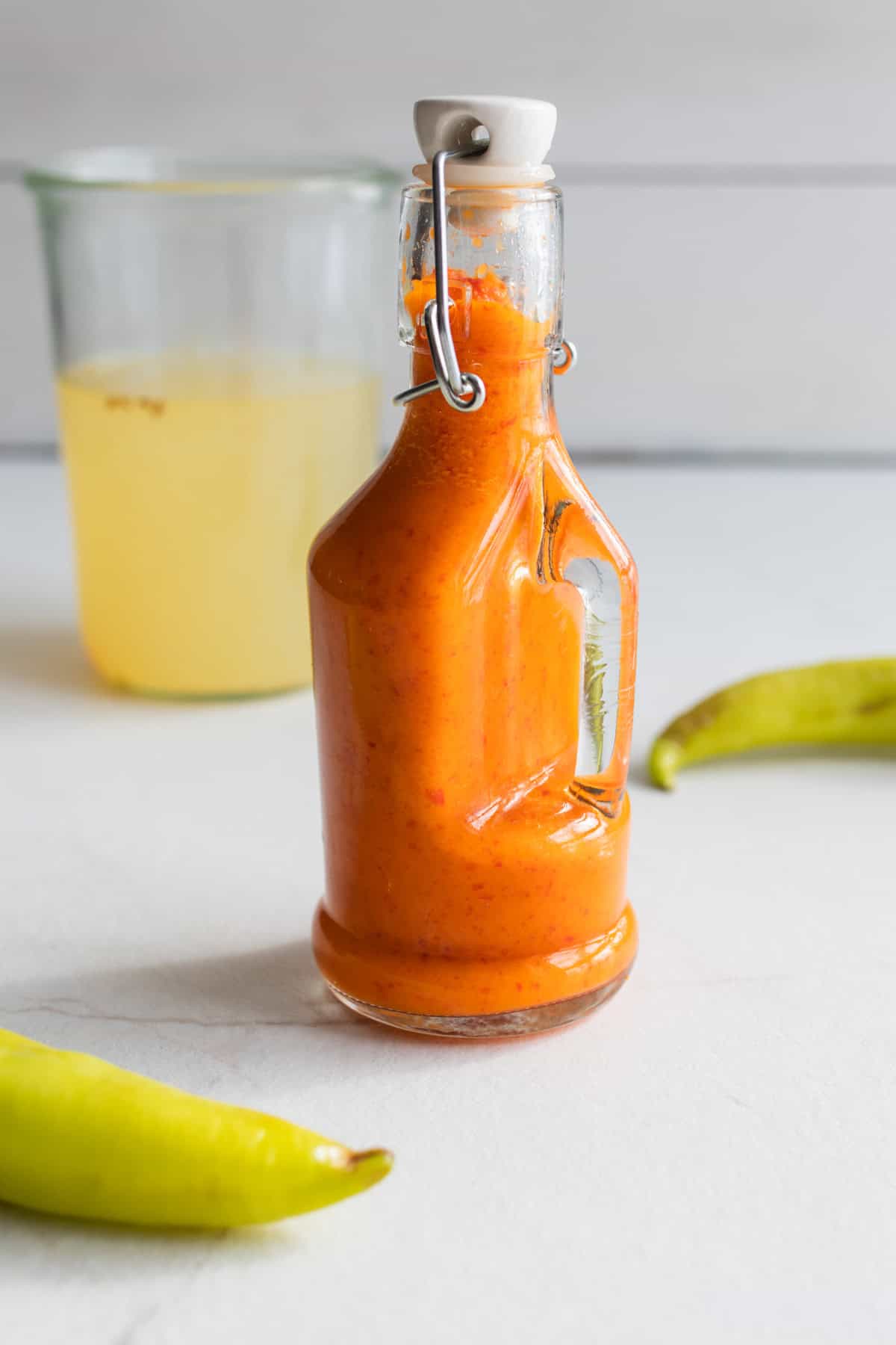 Fermented hot sauce in a swing top bottle surrounded by peppers.