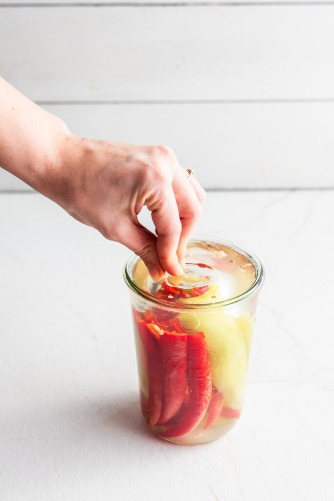 Adding a fermentation weight to peppers with a salt brine.