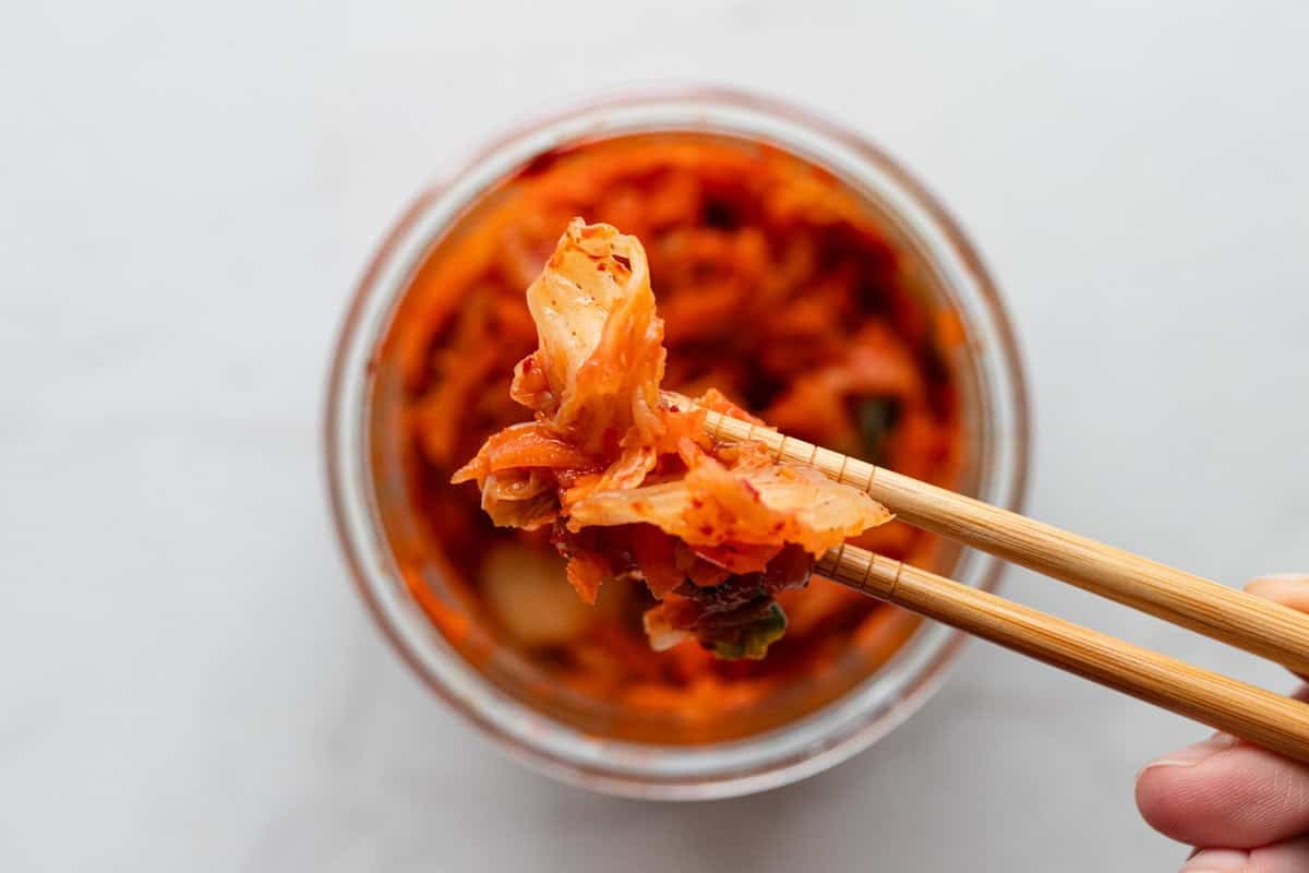 A hand taking out kimchi with chop sticks.