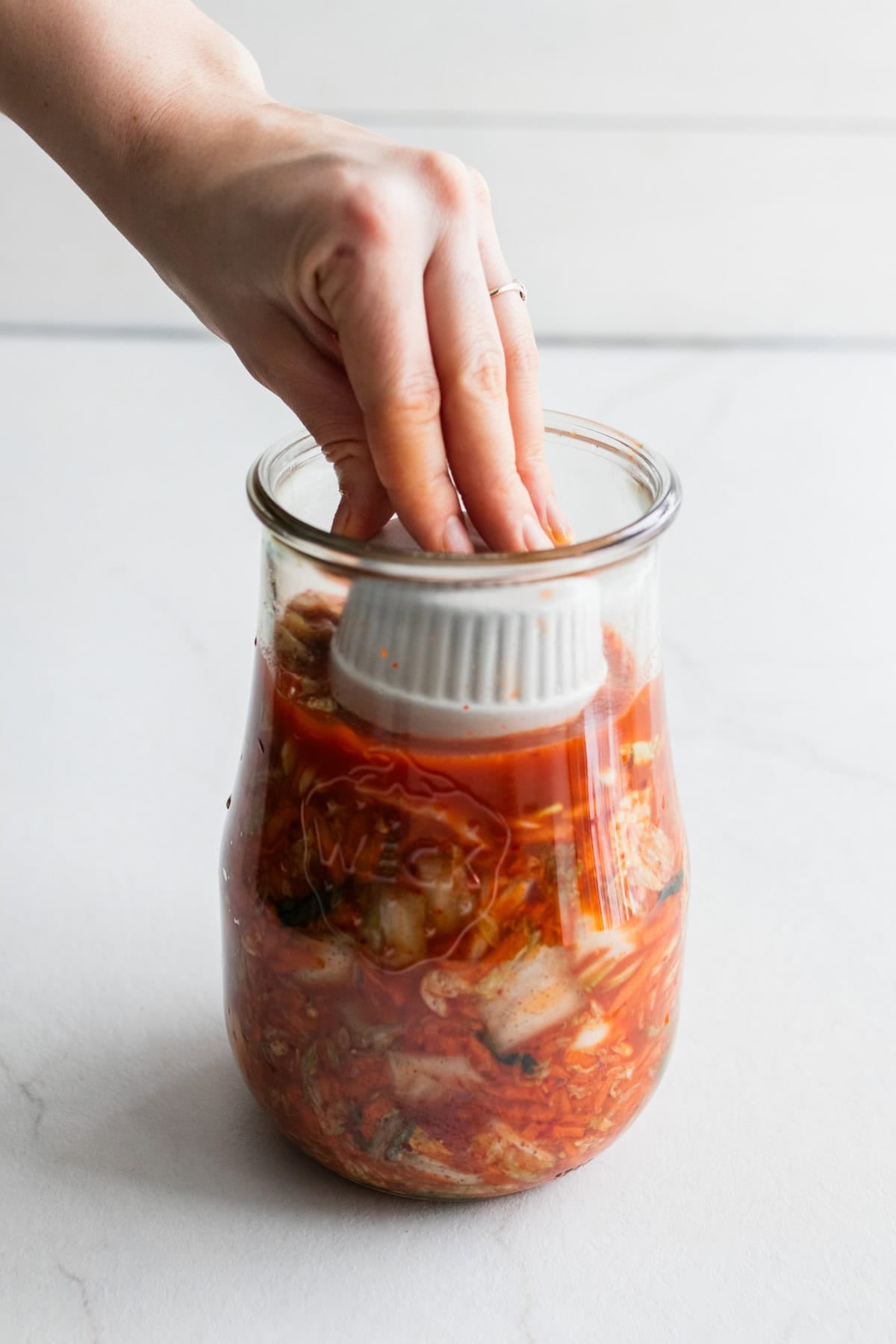 A hand adding a weight to the top of kimchi in a jar.