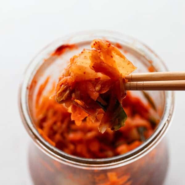 Homemade kimchi in a glass container with chop sticks.