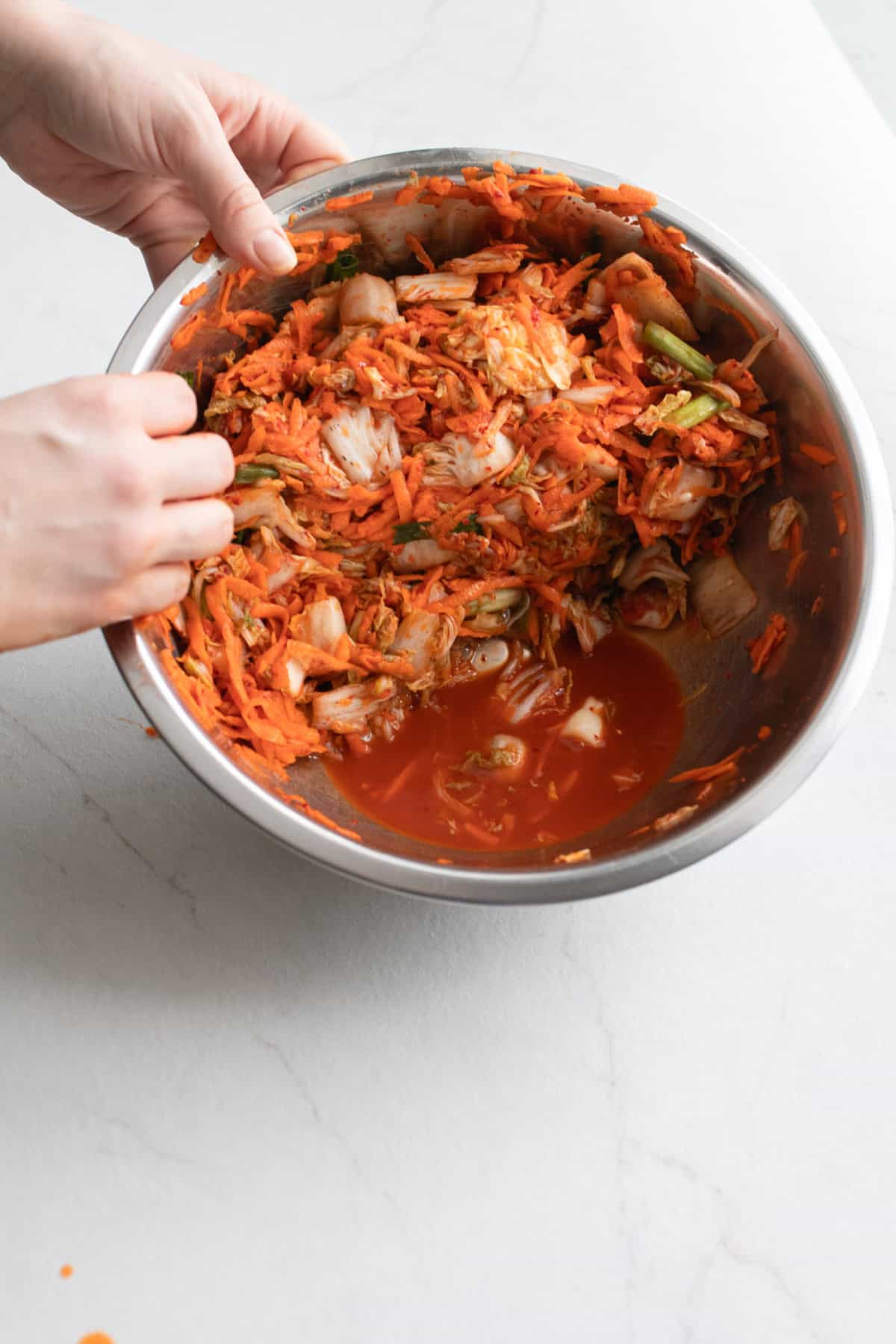 Hands tipping a bowl of kimchi showing the natural brine solution.