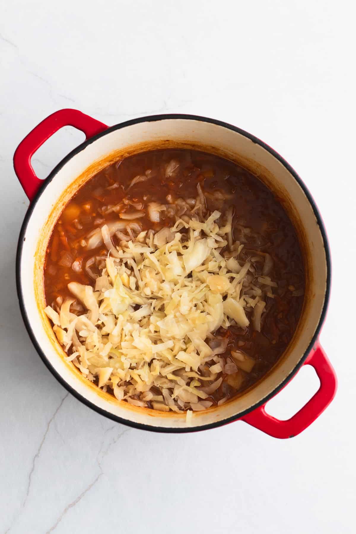 Sauerkraut added to soup in a Dutch oven.