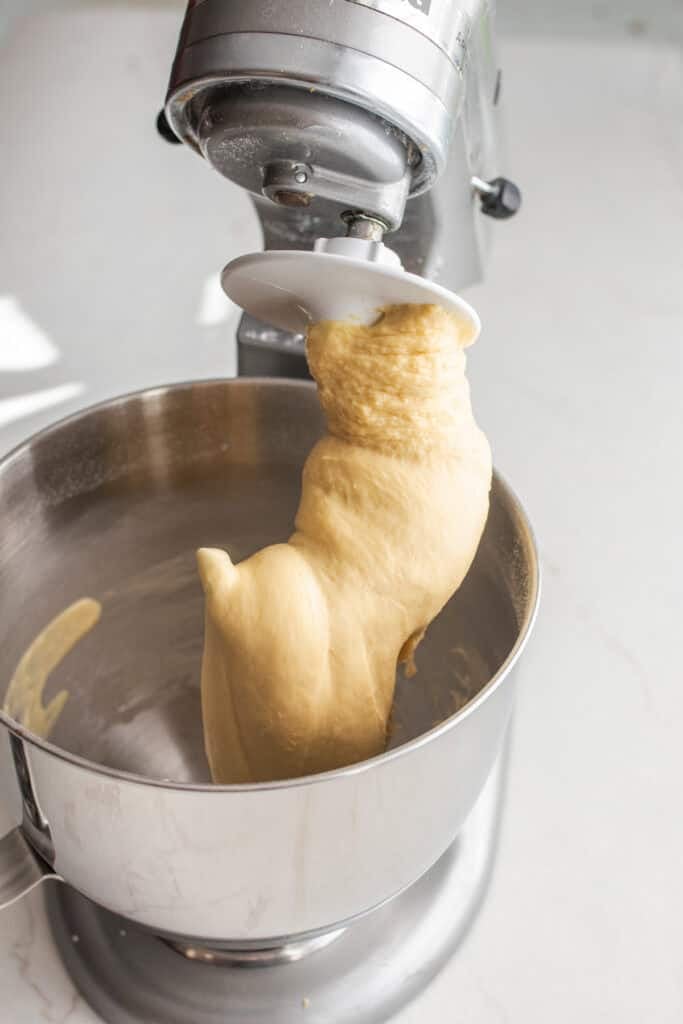 A stand mixer with a dough hook with dough on it. 