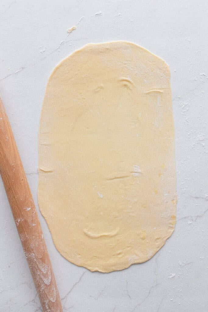 Dough rolled out on a flat surface with a rolling pin next to it. 