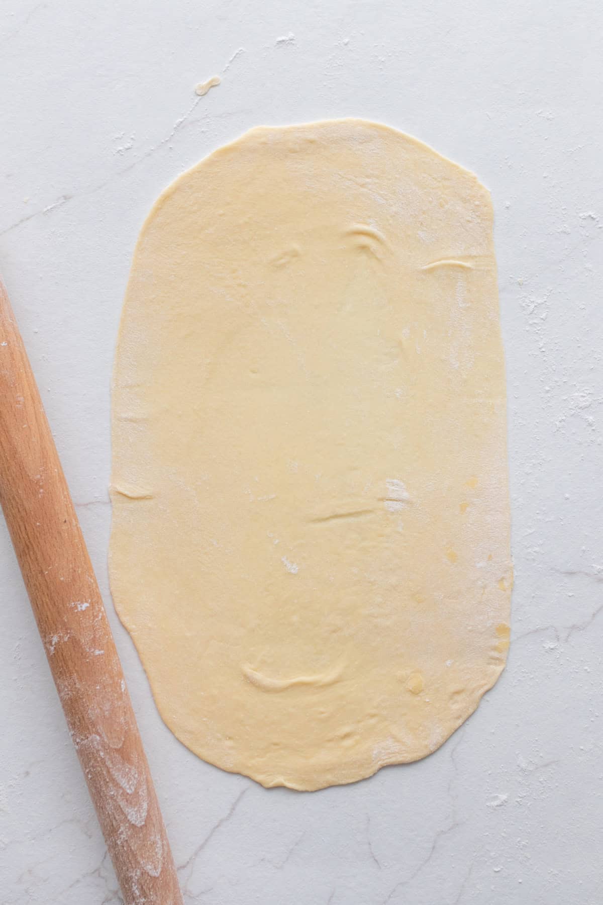 Dough rolled out on a flat surface with a rolling pin next to it.