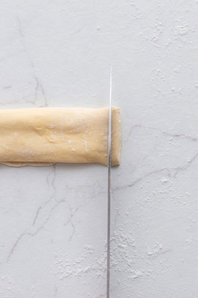 Dough rolled up and being cut with a knife. 