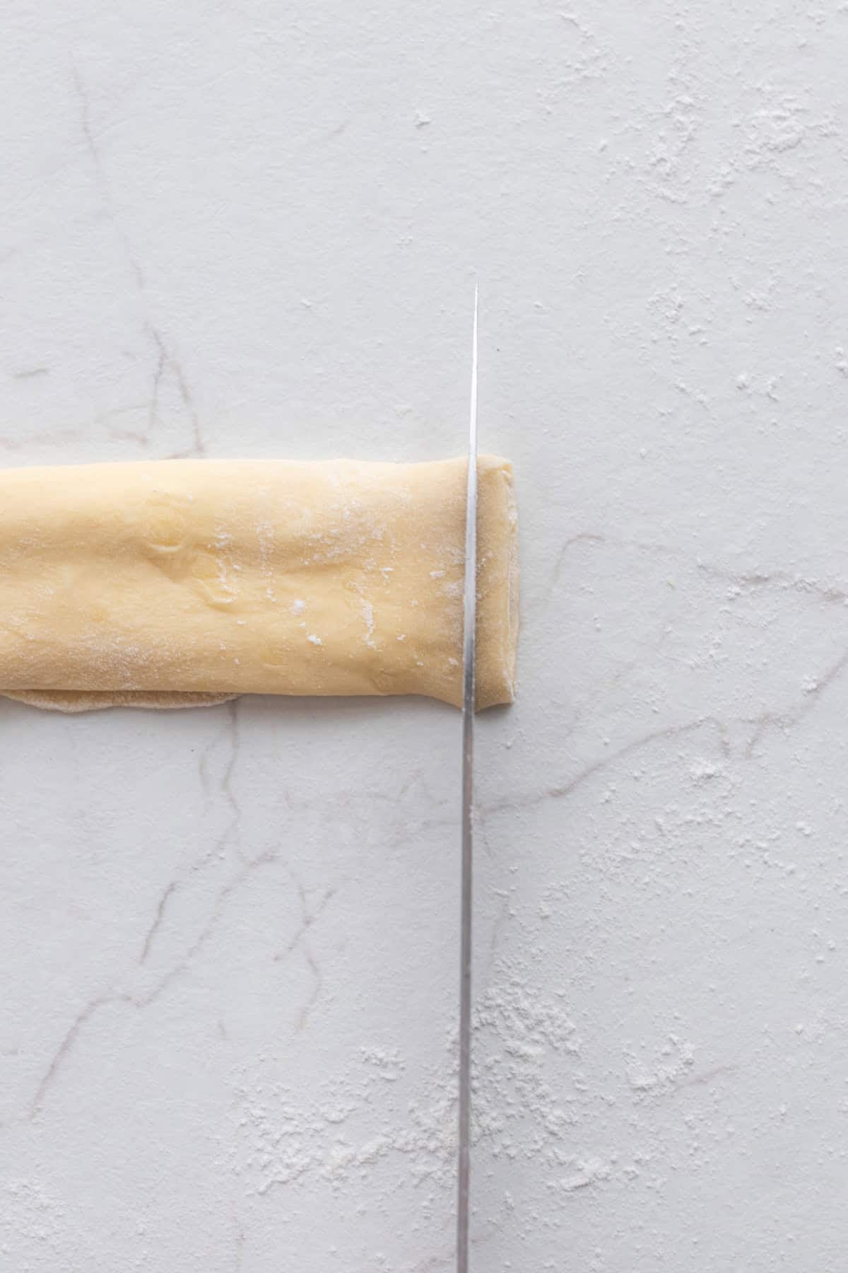 Dough rolled up and being cut with a knife.