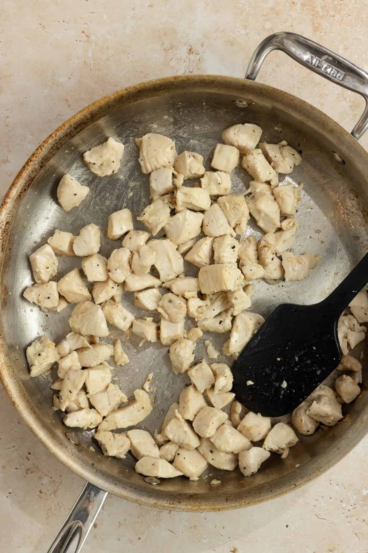 Cubed chicken in a skillet with a spatula.