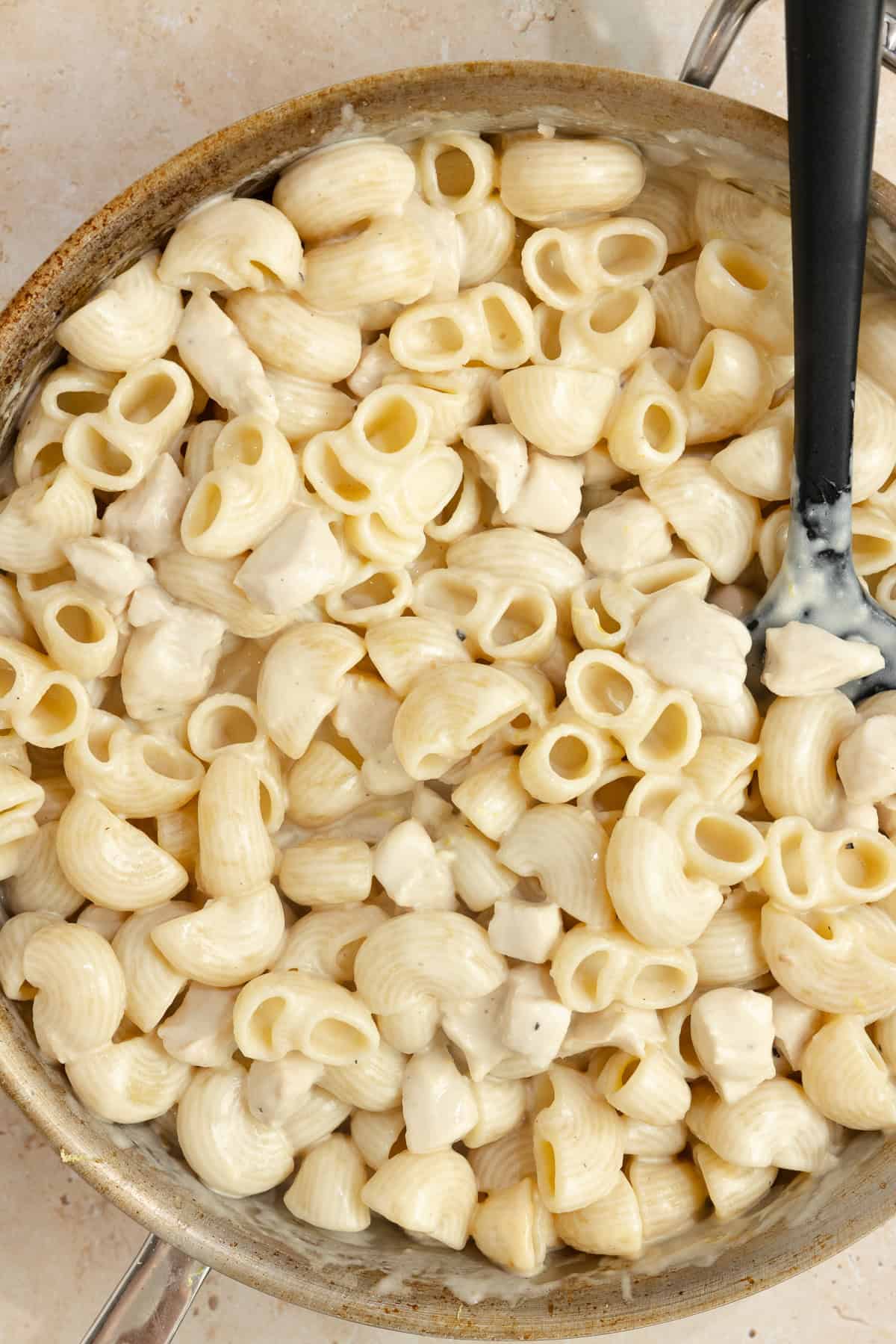 Pasta, chicken, and sauce mixed together with a spatula in a skillet.