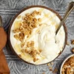 Greek yogurt topped with honey and granola in a bowl with a spoon.