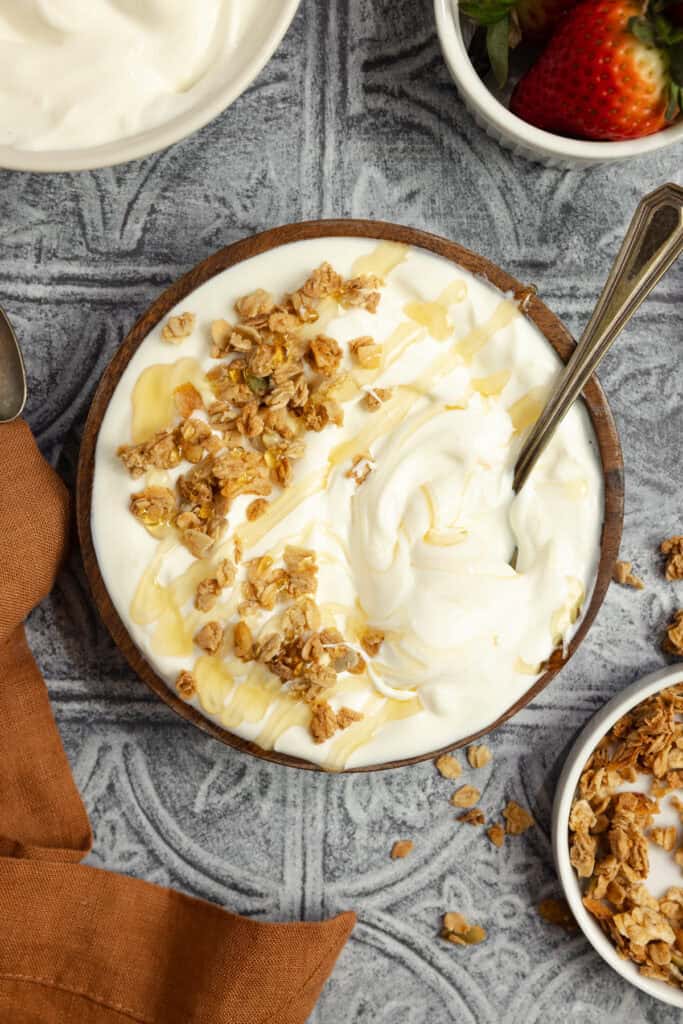 Greek yogurt topped with honey and granola in a bowl with a spoon.