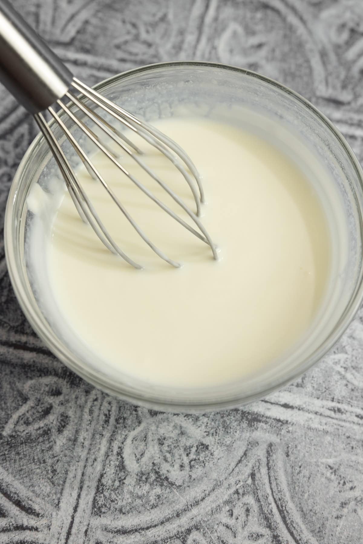 Milk in a glass bowl with a whisk.