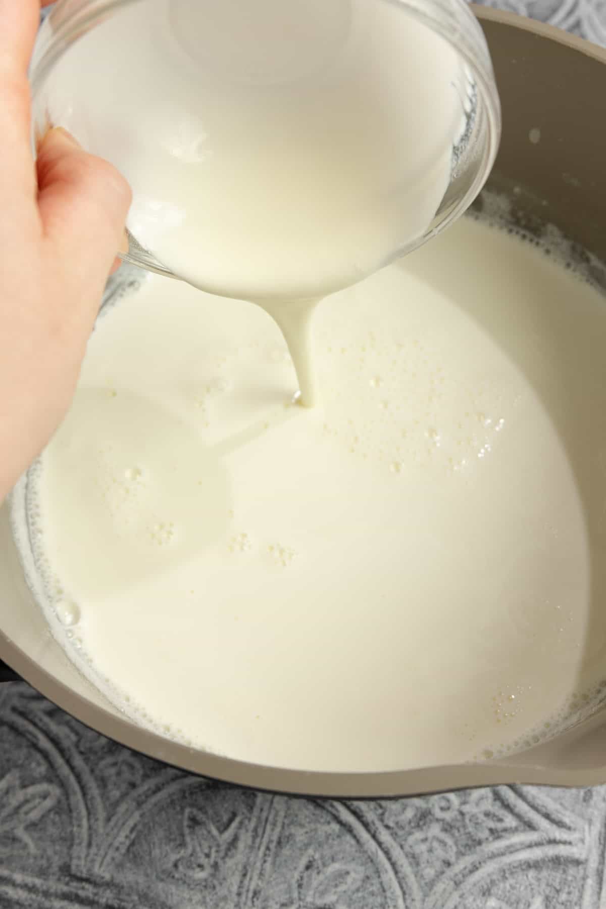 Adding yogurt to a pot of milk.