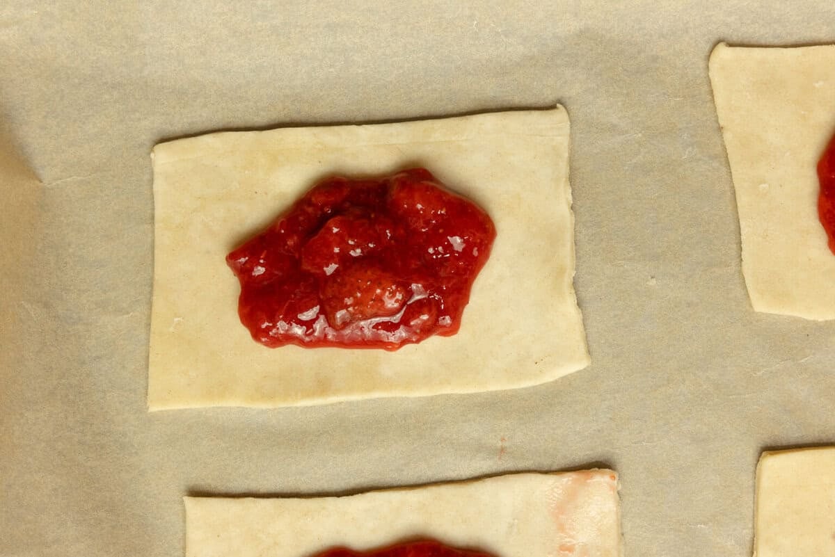 A spoonful of strawberry jam on a rectangle of pie dough.