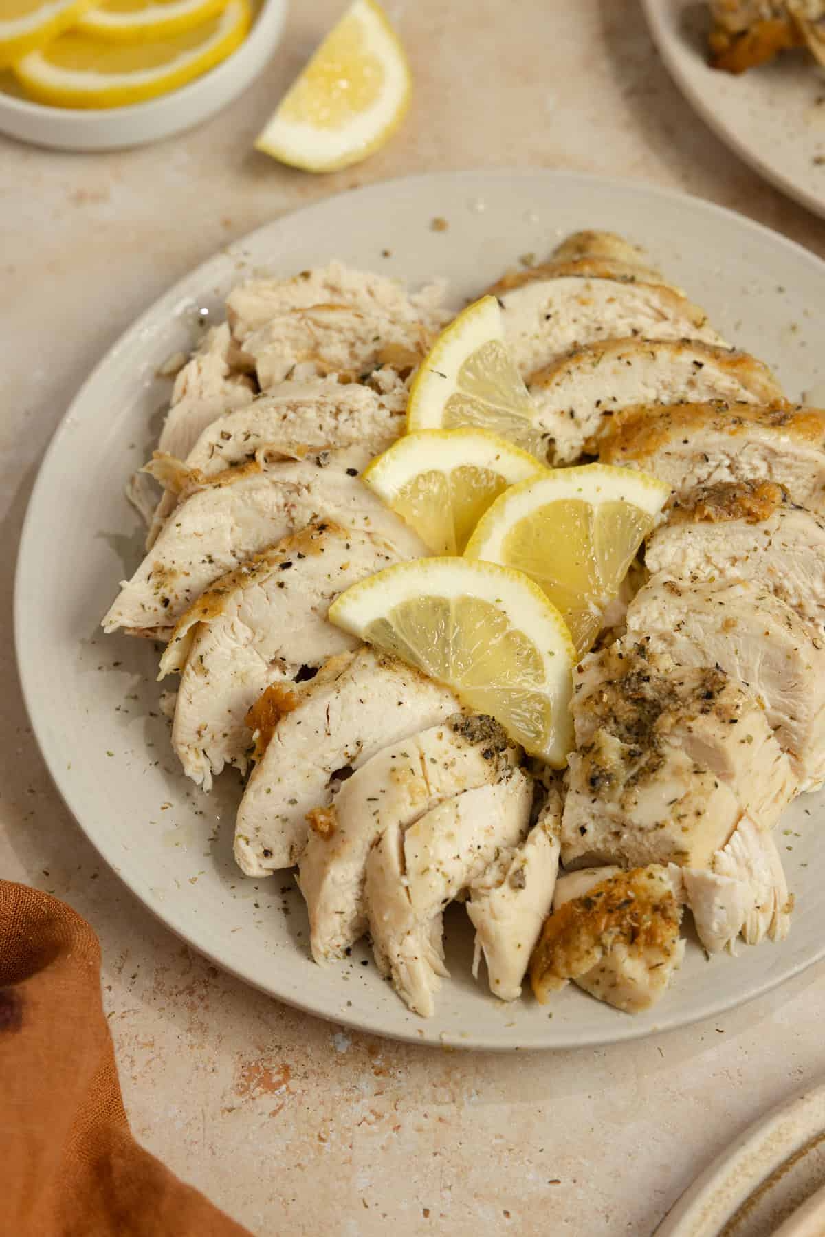 Sliced chicken on a plate with lemon wedges on top.