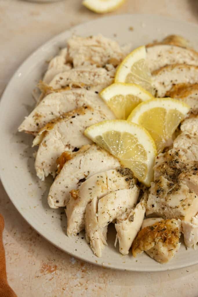 Whole chicken cut up on a plate with lemon wedges on top.
