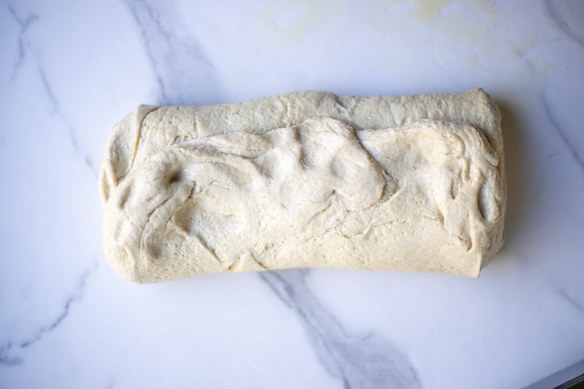 Shaping bread dough on a marble countertop.