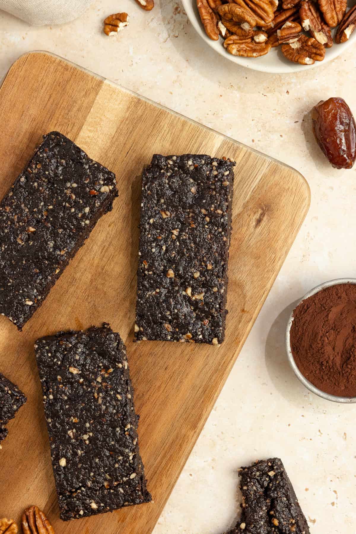 Three homemade larabars on a wood cutting board with ingredients surrounding the board.
