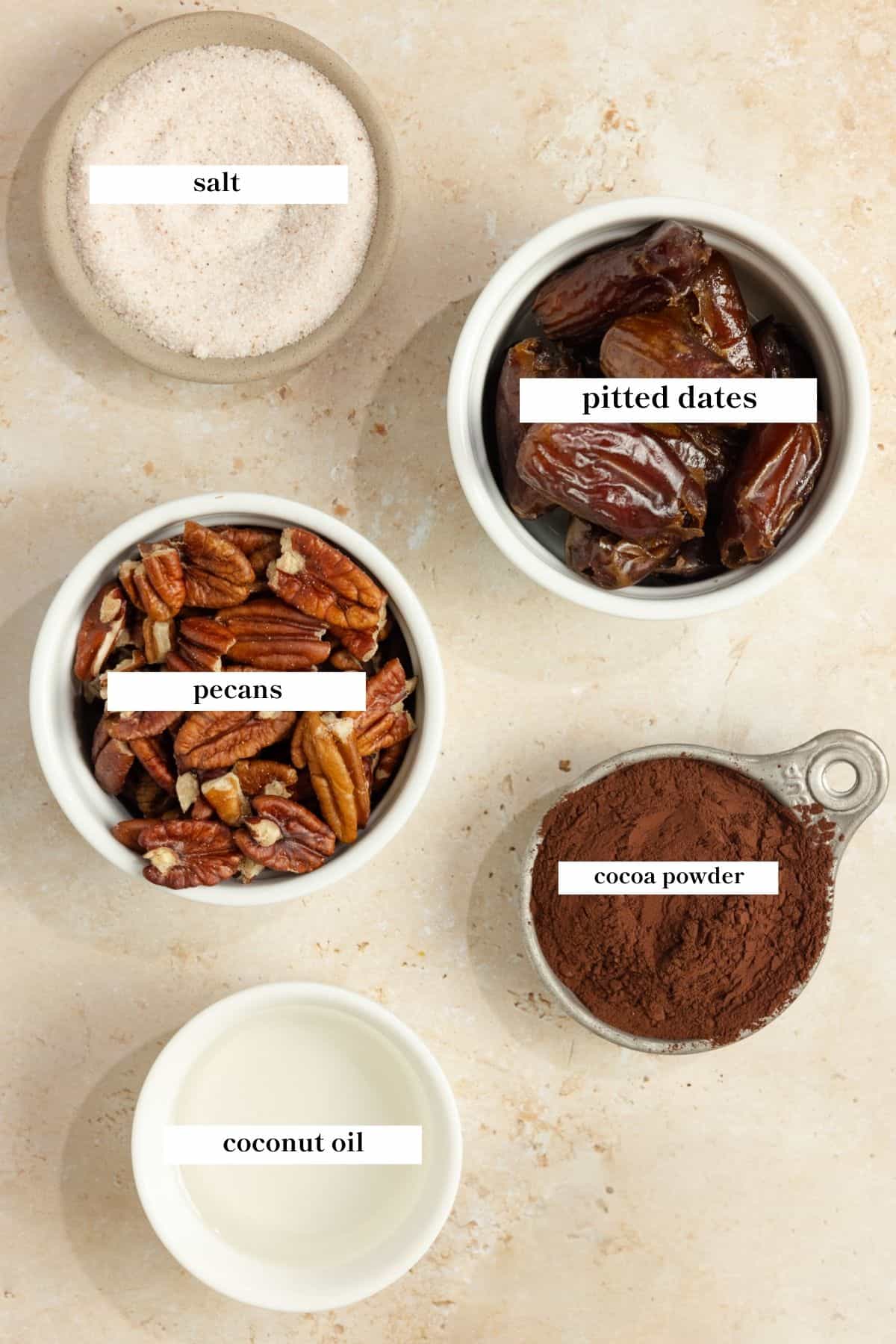 Jars of dates, pecans, cocoa powder, coconut oil, and salt on a countertop.